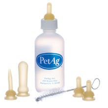 A plastic bottle with a pacifier on top that has a label that reads "PetAG". The bottle is surrounded by four more pacifiers and a metal cleaning brush.